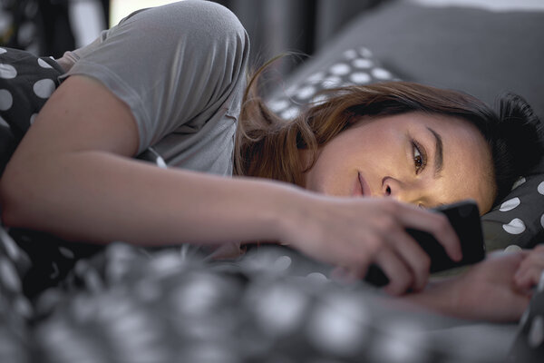 Frau liegt im Bett und schaut auf Handy