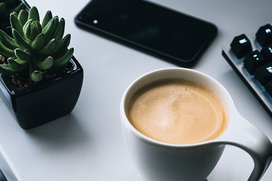 Kaffee Handy und Pflanze am Arbeitstisch