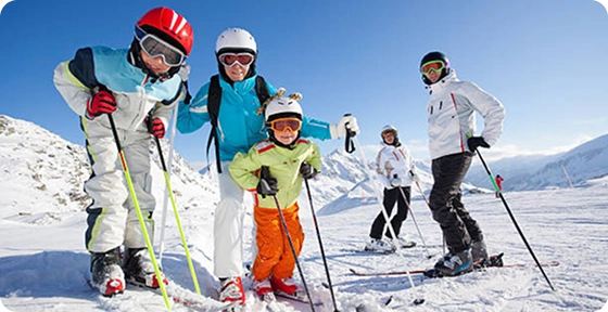Familie og venner på ski smiler på en solrig, snedækket pist