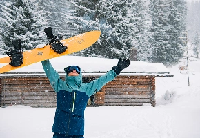 Snowboarder holder et snowboard over hovedet i en snedækket skov